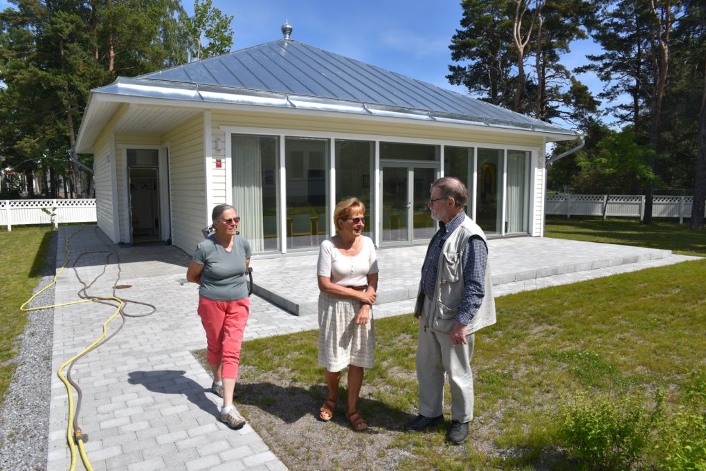 Upouusi seurakuntasali on suunniteltu niin, että lasiseinä tarjoaa täydellisen esteettömän näkymän Hangon kirkkoon. Seurakunta on saanut seurakuntasalin lahjoituksena Hangon kirkon yhteisöltä. Kuvassa etualalla Hangon kirkon ystävät ry:n jäsen ja seurakunta-aktiivi Eeva Pellonma (vas.), Hangon kirkon vahtimestarin tehtävässä kesäkuussa aloittanut vahtimestari Tuuli Santakari, jo yli kaksikymmentä vuotta Hangon kirkon isännöitsijänä toiminut Alan Jeffrey.